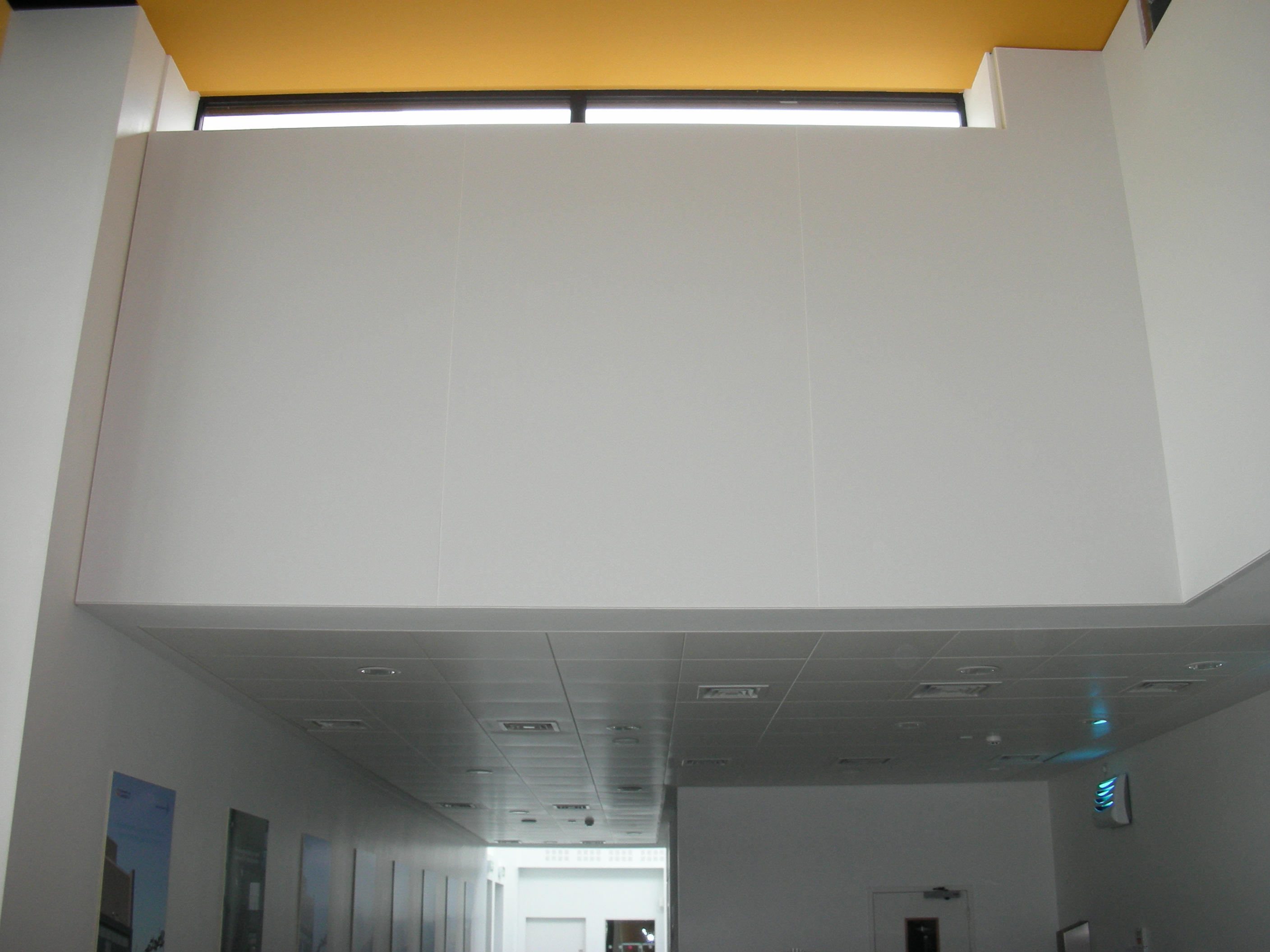 Interior view of a modern building with a high ceiling, white walls, and a yellow ceiling accent