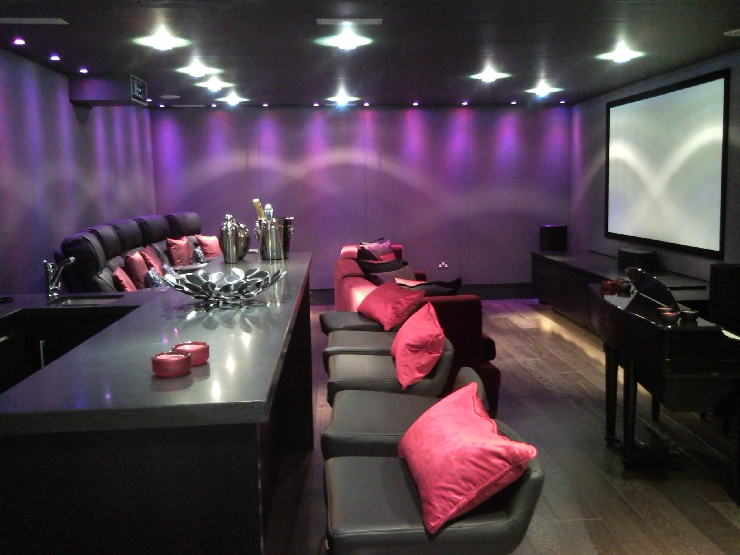 A luxurious home theater with purple lighting, comfortable seating, and a large screen