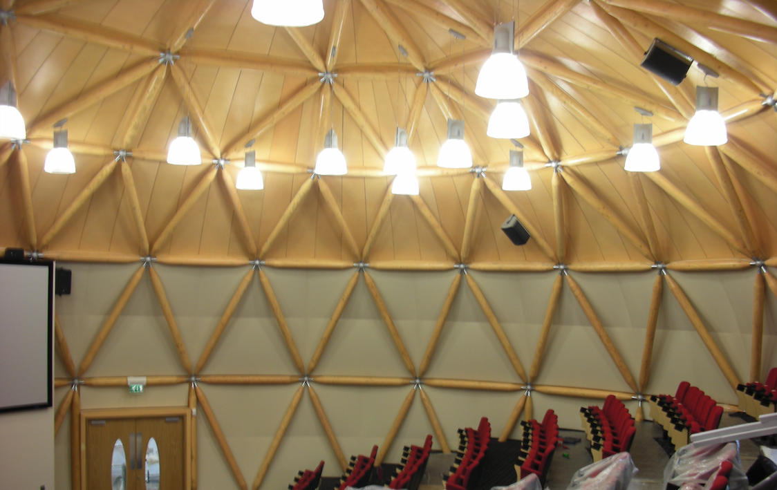 Interior of a geodesic dome auditorium with wooden beams and red seating